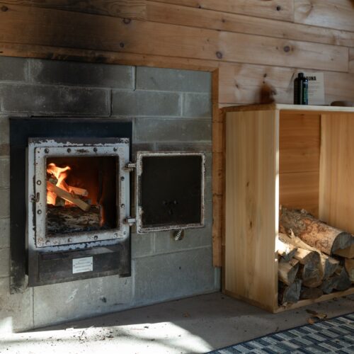 Wood-fired warmth: the sauna stove burning bright with plenty of logs ready for your next session.