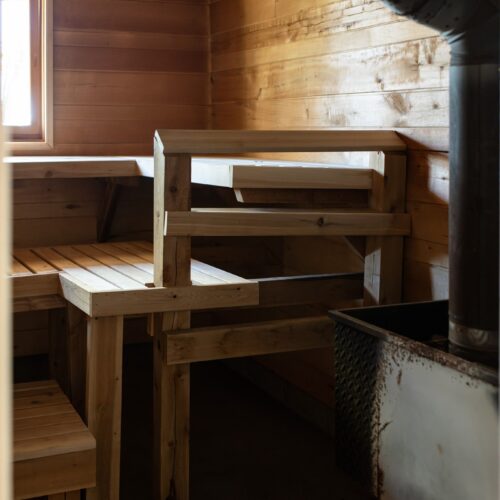 Spacious cedar sauna with seating for eight, a glowing stove, and serene lake views.